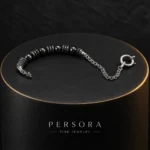 دستبند هایبرید حدید و زنجیر با قفل ملوان Gunmetal Hematite & Chain Sailor Bracelet با مهره های حدید گان متال مشکی براق و اسپیسیر های نقره ای طرح دار آنتیک و زنجیر استیل و قفل ملوانی حلقه ای نقره ای روی استند استوانه ای مشکی مات با لبه طلایی و لوگوی PERSORA FINE JEWELRY با نورپردازی لوکس