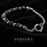 دستبند هایبرید حدید و زنجیر با قفل ملوان Gunmetal Hematite & Chain Sailor Bracelet با مهره های حدید گان متال مشکی تراش دار براق و اسپیسیر های نقره ای آنتیک طرح دار و زنجیر استیل رولو و قفل ملوانی حلقه ای نقره ای کلوزآپ روی پارچه مخمل مشکی با لوگوی PERSORA FINE JEWELRY و نورپردازی لوکس