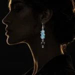 گوشواره آویز هندسی آکوامارین و اونیکس نئو مینیمال با مهره های چیپسی آکوامارین آبی روشن و مروارید اونیکس مشکی براق و قلاب نقره ای روی گوش مدل زن با نورپردازی نیم رخ دراماتیک و پس زمینه مشکی