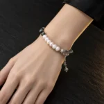 دستبند هایبرید مروارید باروک و عقیق خزه ای نئو مینیمال با قفل تاگل و آویز دو مهره ای روی مچ دست زنانه