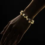 دستبند راف سیترین و بند گره باف Raw Citrine Knotted Bracelet با خوشه های سنگ راف سیترین زرد عسلی شفاف و بند بافت مشکی گره ای و قفل خرچنگی استیل روی مچ دست زن در تاریکی با نورپردازی طلایی سایه دار و پس زمینه مشکی دراماتیک